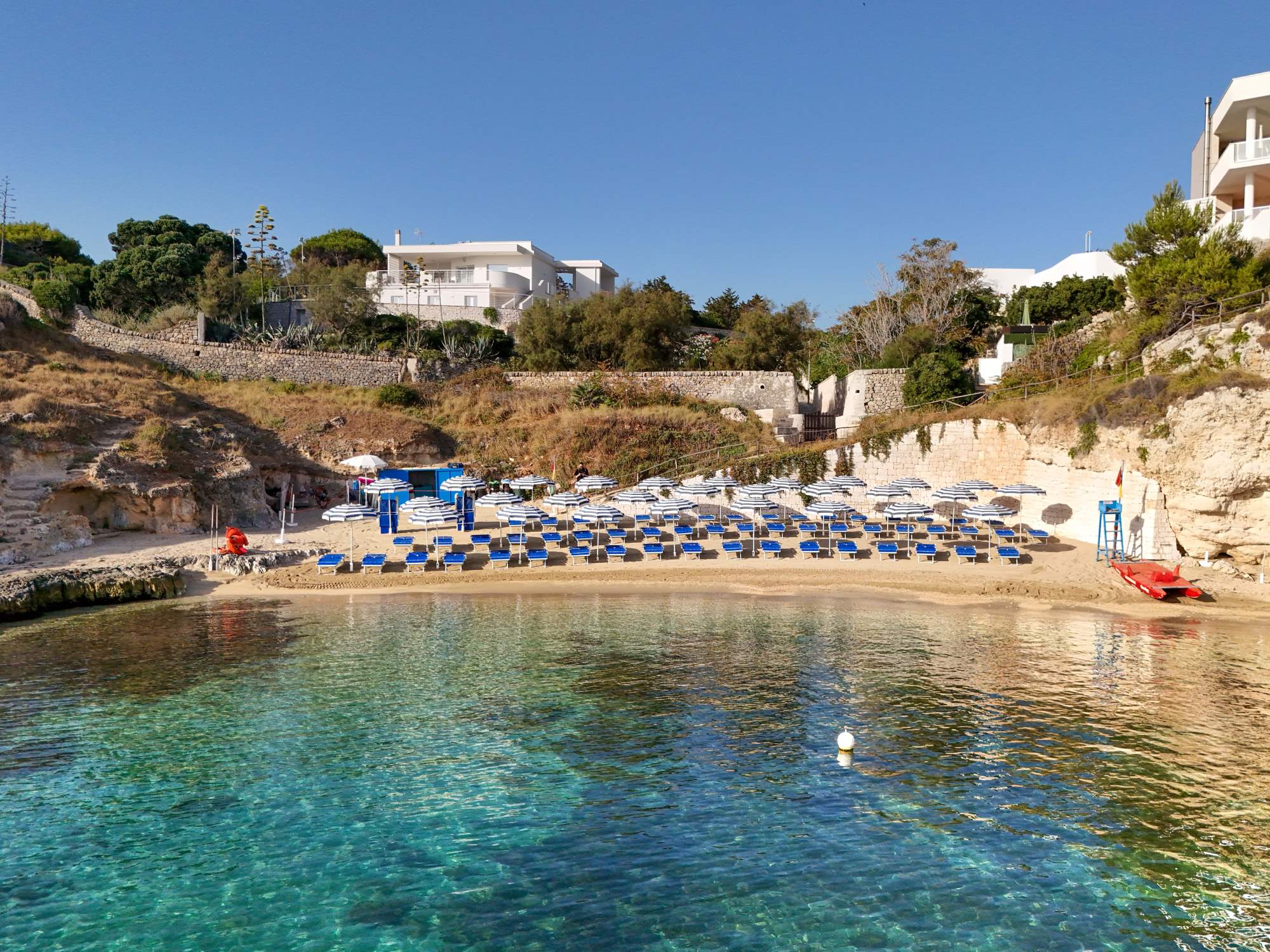 Caletta di Cala Corvino vista dal mare con ombrelloni, lettini e acqua cristallina a Monopoli